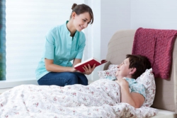 caregiver reading a book to her elderly patient who is sick